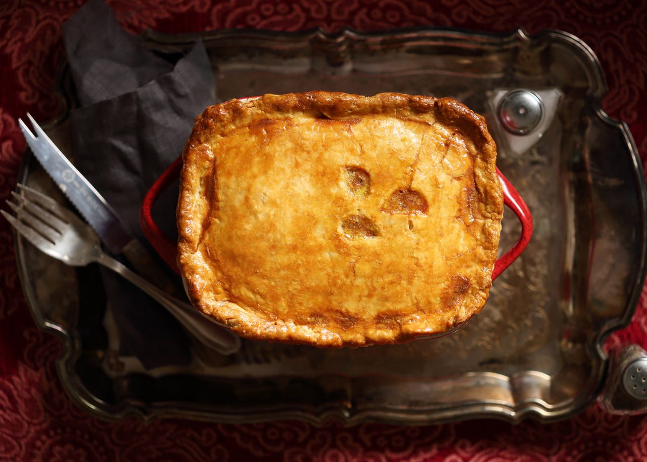 A pot pie on a serving platter with cutlery and salt and pepper shakers
