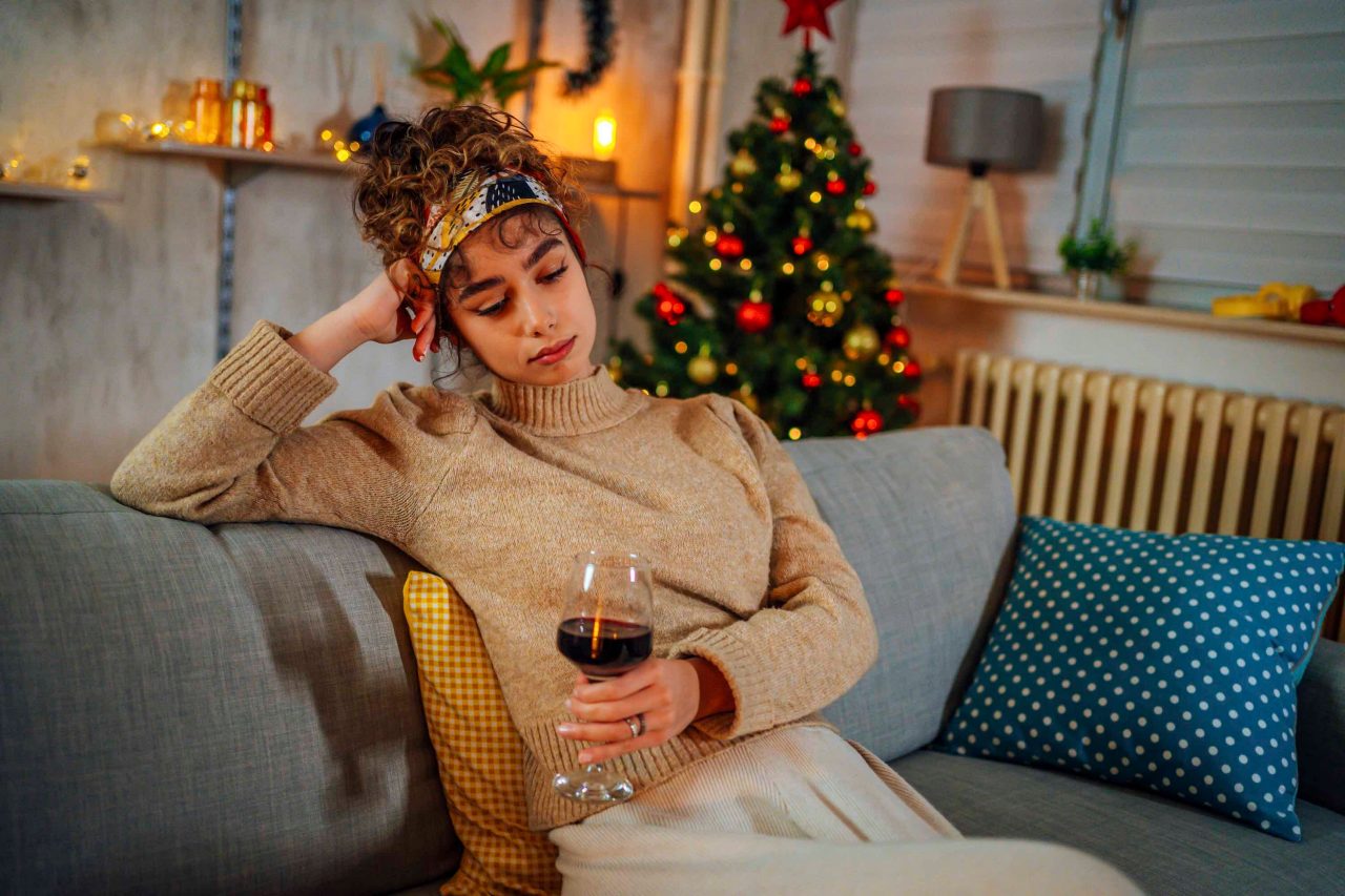 Young lonely woman drinking red wine during Christmas holiday