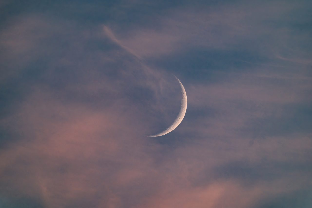 Crescent moon adorned by red clouds during a sunset. A beautiful capture that can be used as a background. Taken with a high-quality telephoto lens