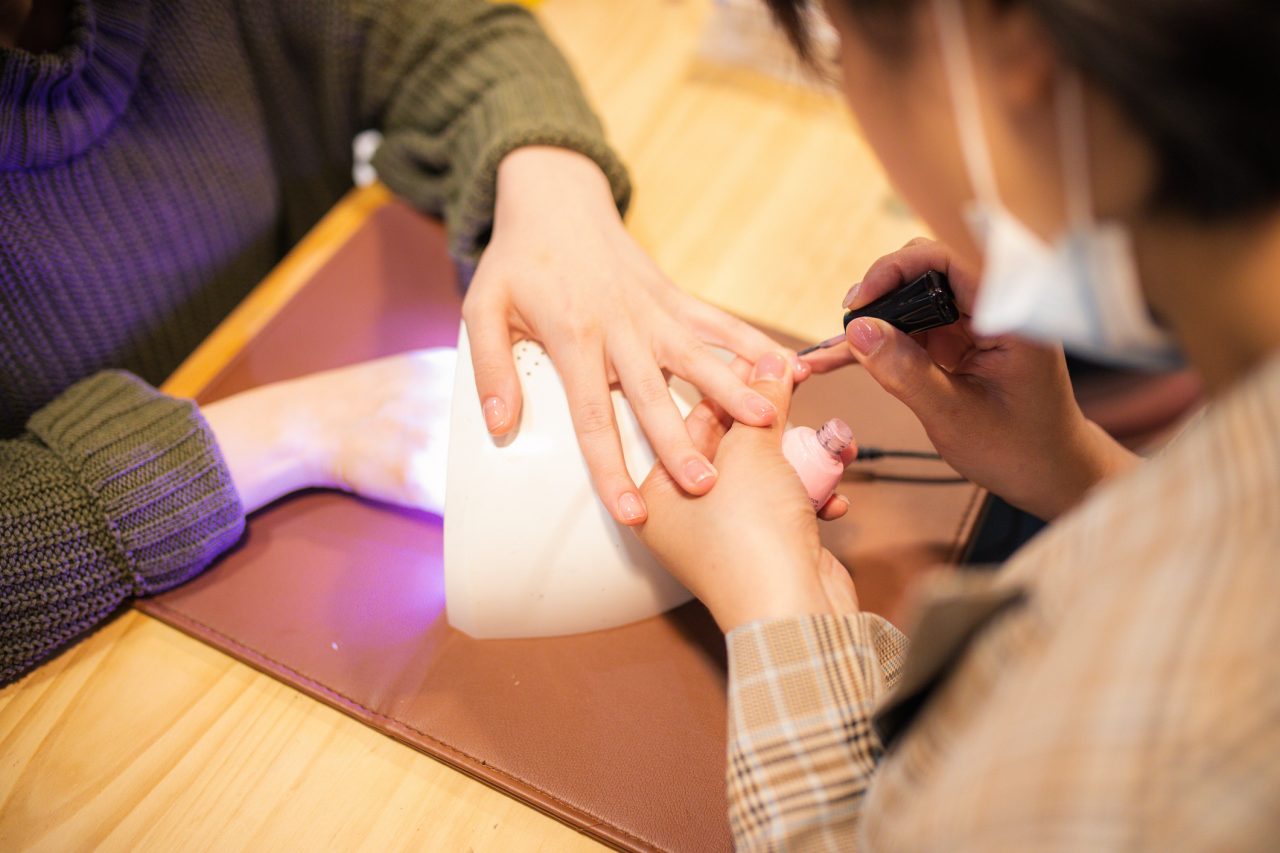 Close up of woman's hand under UV Nail Dryer, while manicurist applying nail polish on other hand