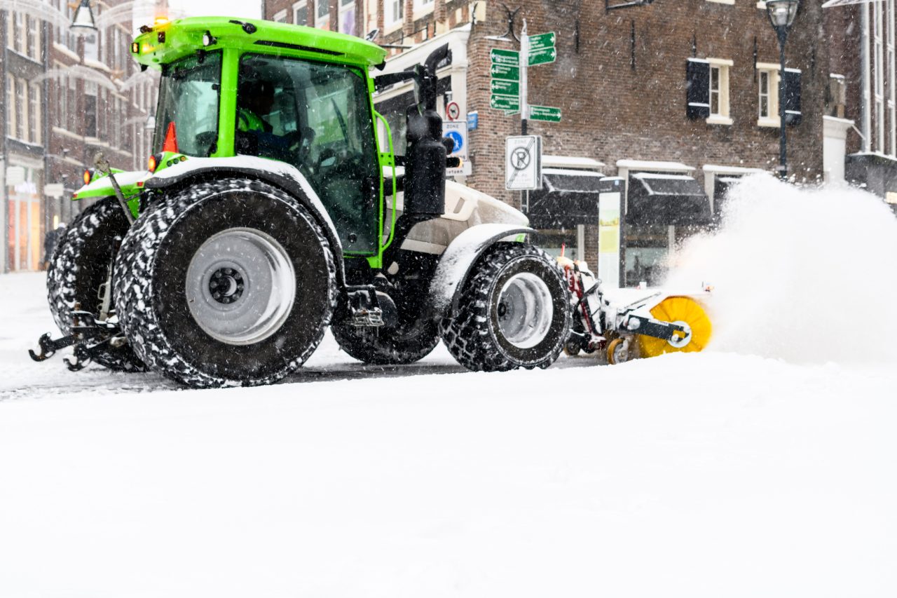 Tractor clearing the streets of snow with a snow plow and brush after heavy snowfall in the streets of Zwolle during a cold winter day.
