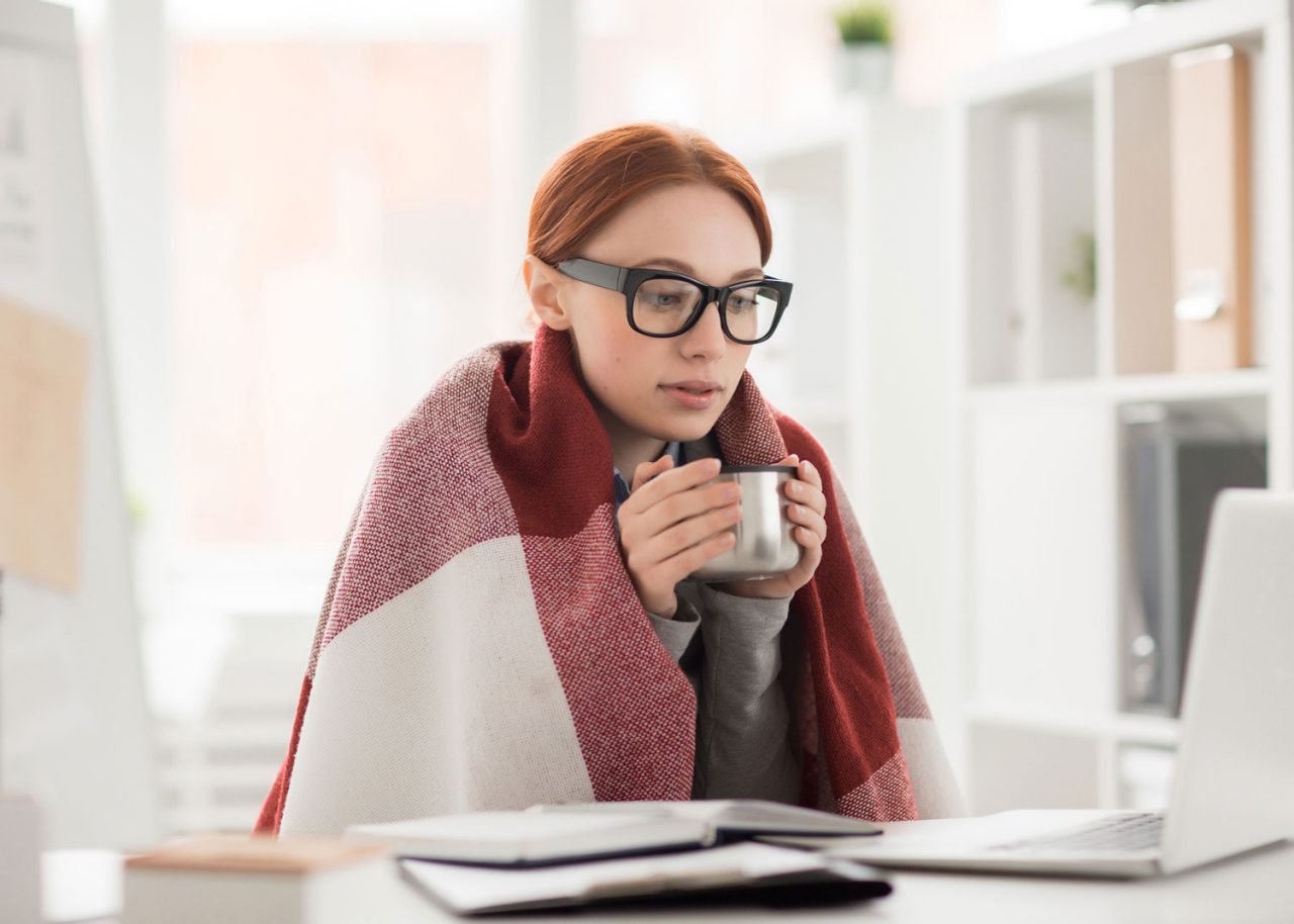 femme avec couverture et café a froid au bureau devant son ordinateur