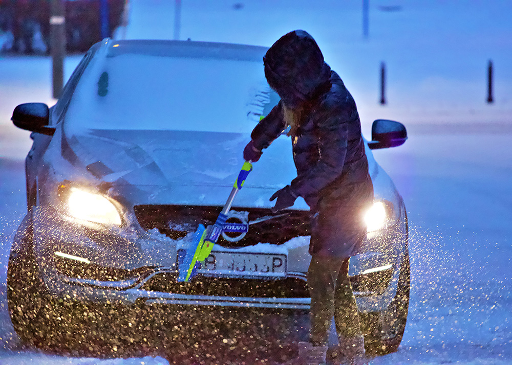 Une femme déneige sa voiture en hiver