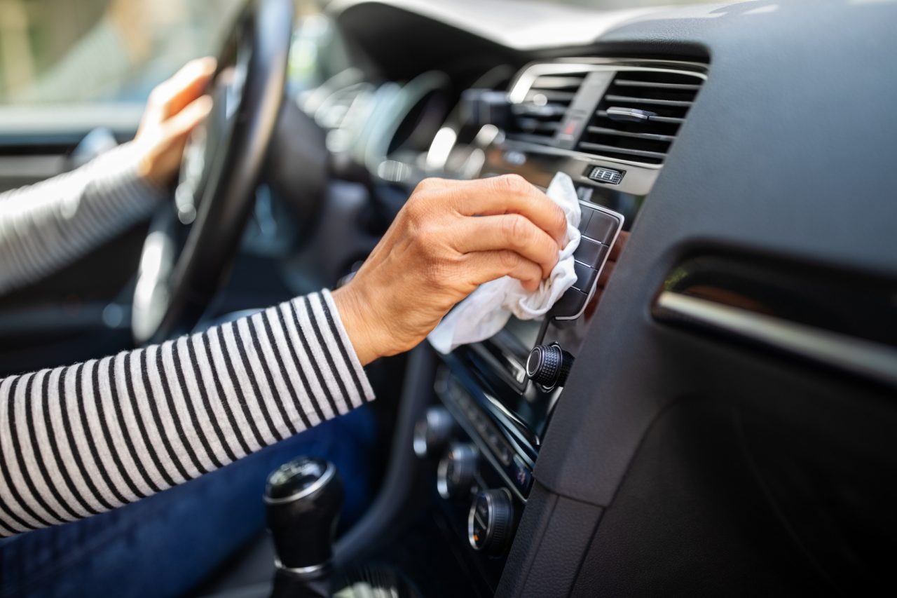 Close-up of a woman with tissue paper cleaning and disinfecting her car interior during corona virus outbreak. Focus on female hands cleaning car with wet wipes to prevent from corona virus outbreak.