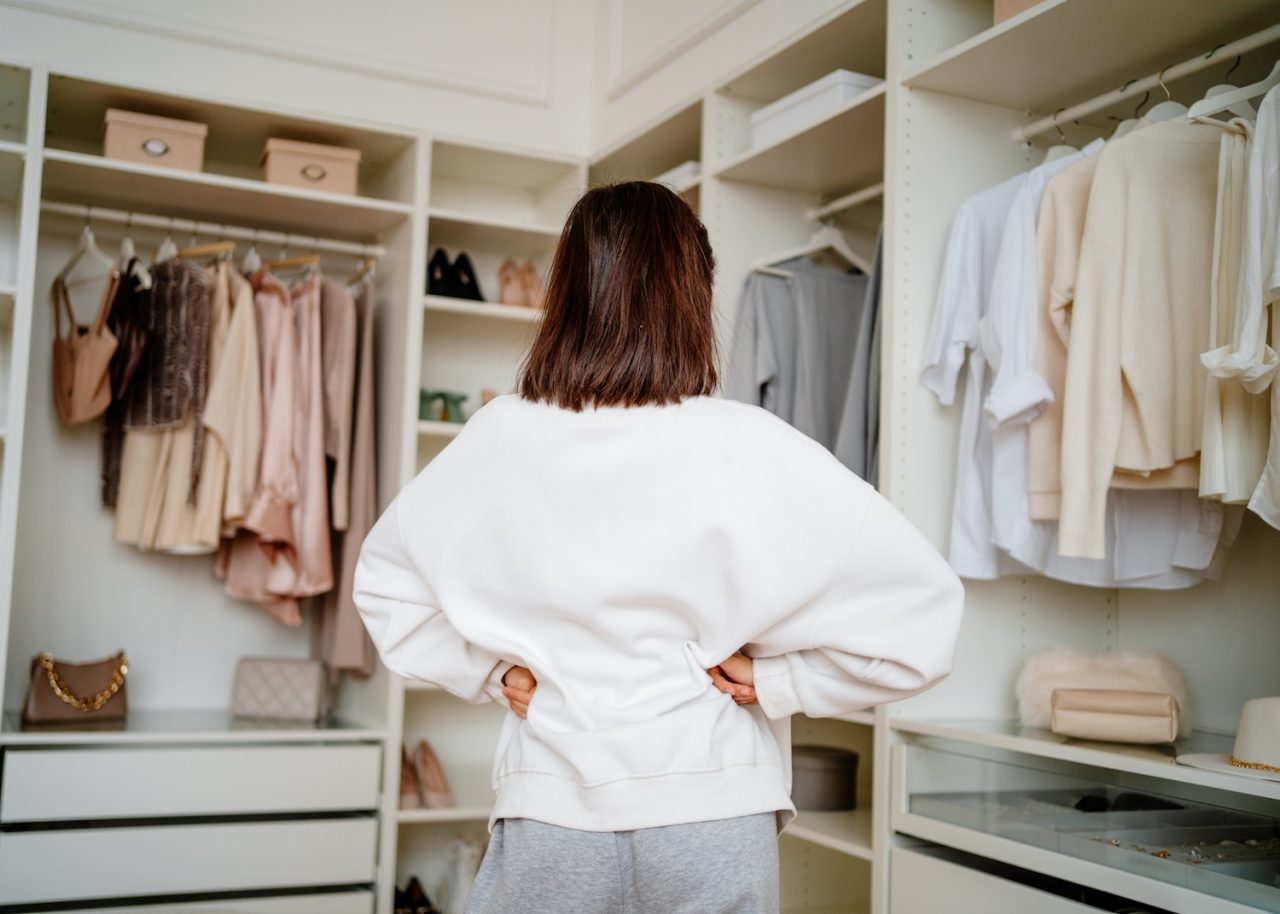 Woman with hands on hips looking at her clothes in the closet room