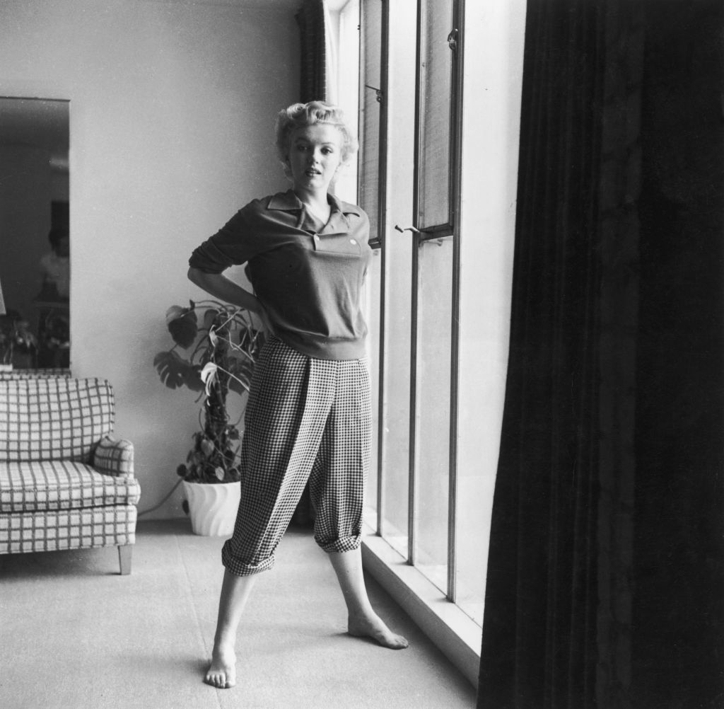 circa 1955:  American actor Marilyn Monroe (1926 - 1962) stands barefoot near a window in a sweater and checkered pants.  (Photo by Hulton Archive/Getty Images)