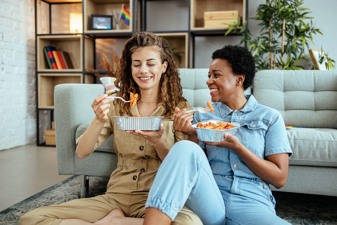 Lesbian couple relaxing at home and eating pasta