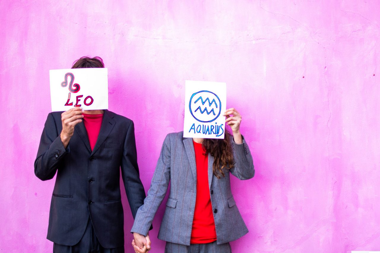 a young couple holding a sign with their zodiac sign. Hidden face, unrecognizable person. Pink background.