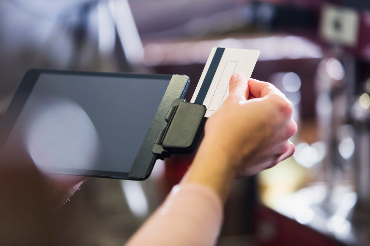 Close up of a female hand swiping a credit card or gift card through a reader attached to a digital tablet.