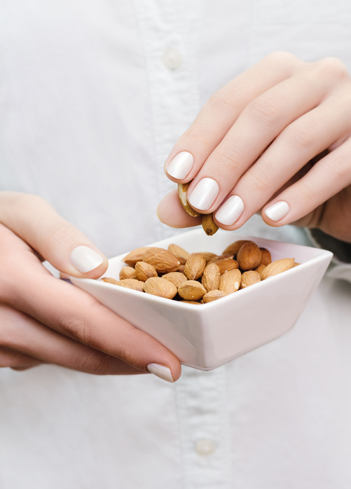 Almonds in white bowl on woman hands.
