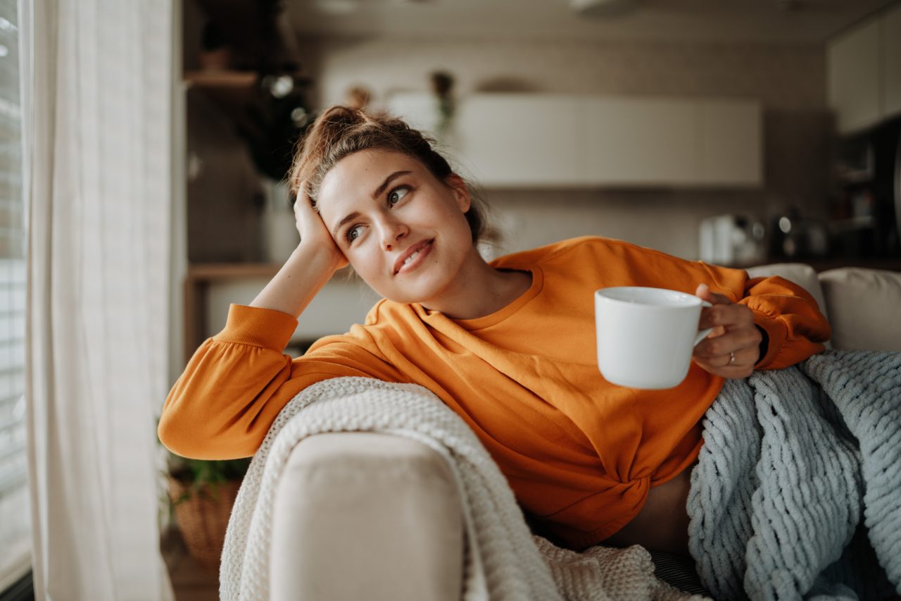 Young woman resting on sofa with blanket and cup of tea.
