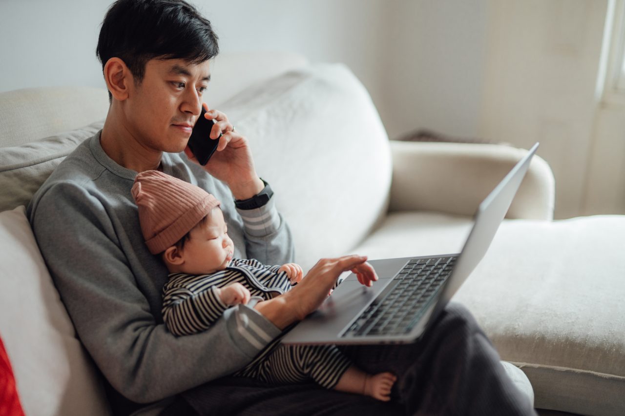 Businessman working from home while taking care of his baby. Father balancing work and family life concept.