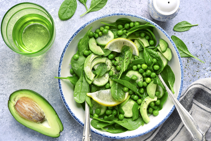 Spring salad with green vegetables : avocado, sweet pea, cucumber and baby spinach in a vintage bowl on a light grey slate, stone or concrete background.Top view.