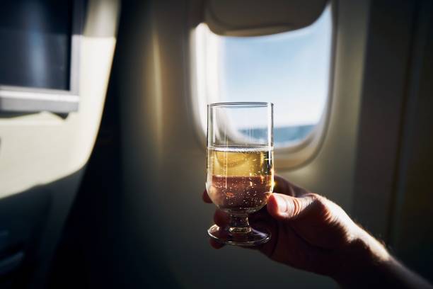 Dring during flight. Man holding glass of sparkling wine against airplane window.